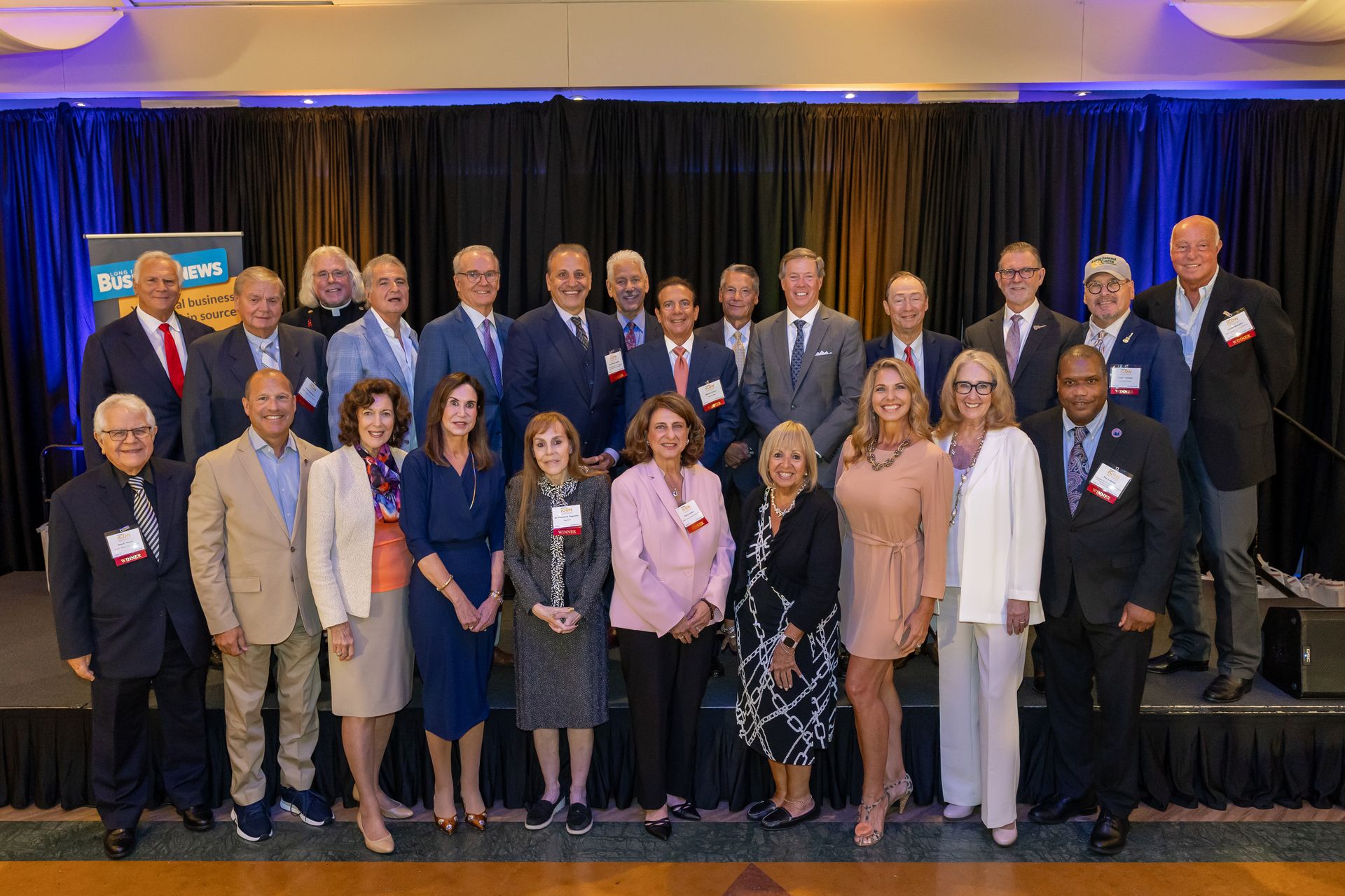A large group photo of the 2025 Icon Honors award recipients and attendees posing together on a stage in front of dark curtains.