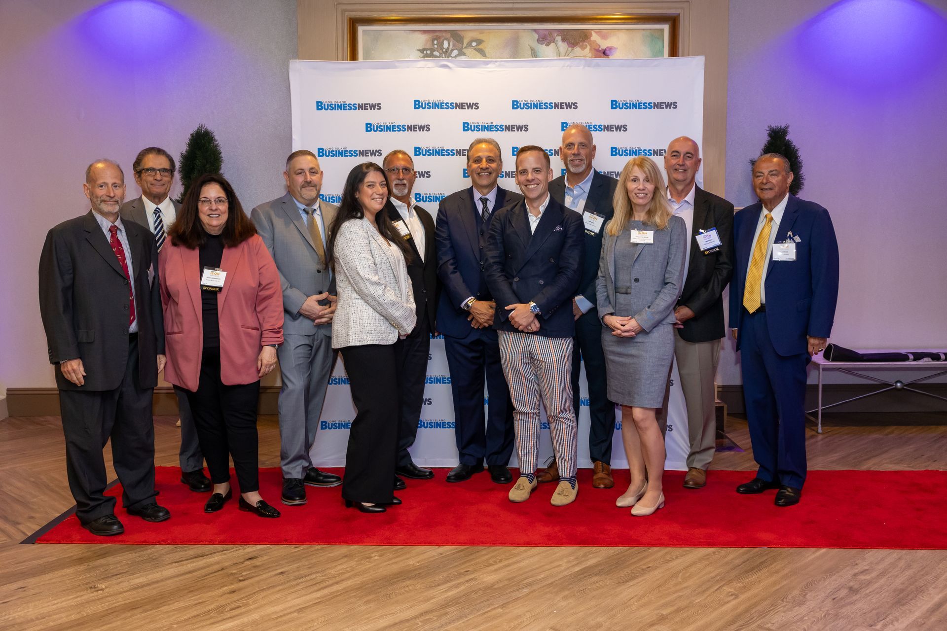A group of professionals standing on a red carpet in front of a Long Island Business News backdrop for a photo opportunity.
