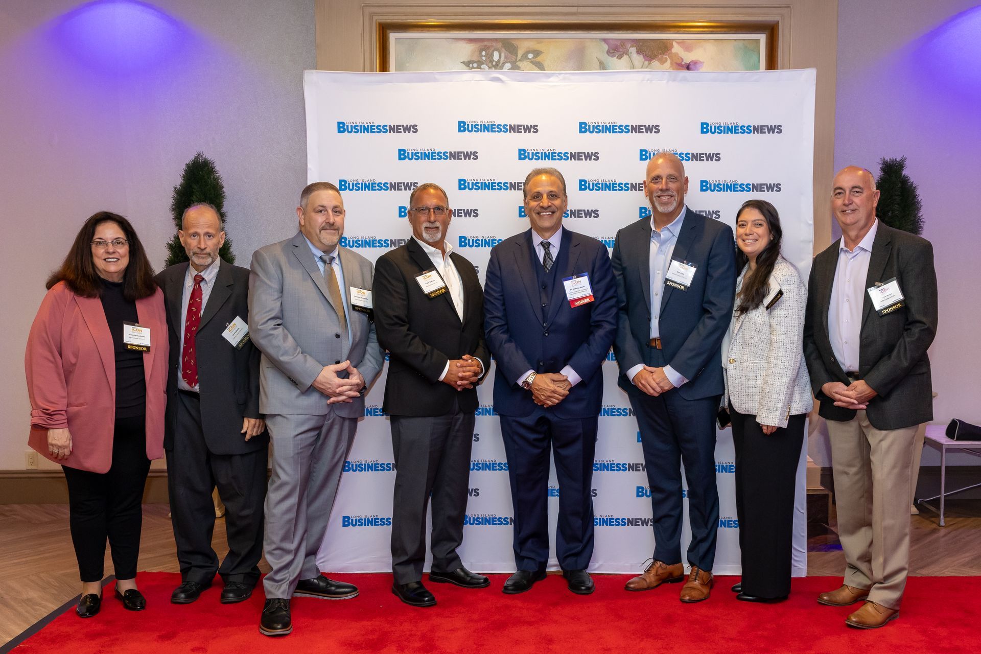 A group of colleagues standing together on a red carpet in front of a Long Island Business News media wall.