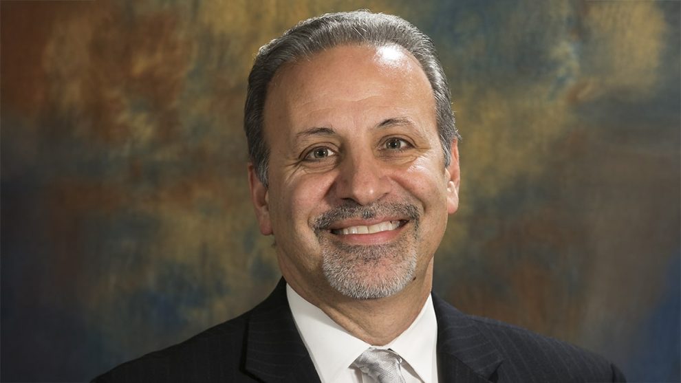 Smiling man in a suit against a softly blurred background. His confident demeanor suggests professionalism and approachability, suitable for a business profile.